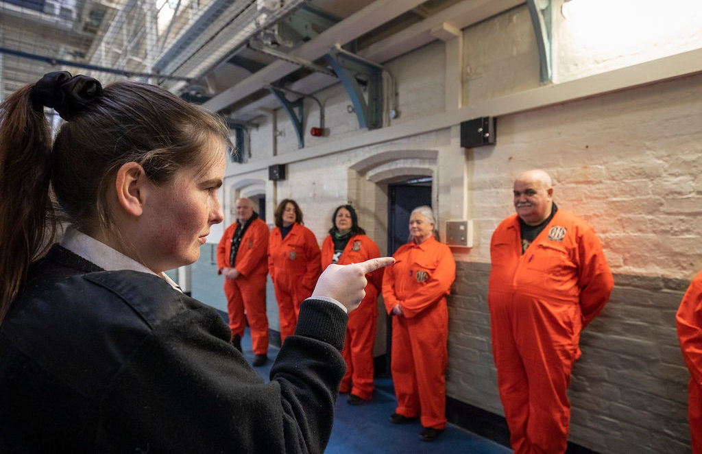 An officer pointing at visitors in orange jumpsuits during Prison Break